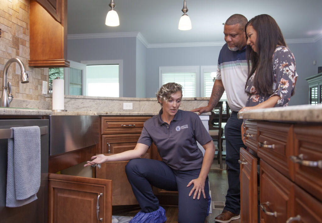 Meetze plumber looking under a sink & talking to clients